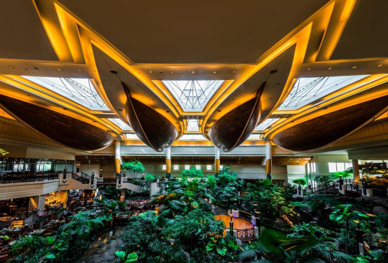 Grand Hyatt Dubai Hotel Exterior photo The photo depicts the interior of a grand building, likely a hotel or resort, featuring a stunning atrium. The space is characterized by large, elegantly designed boat-shaped structures suspended from the ceiling, which are illuminated by warm light.