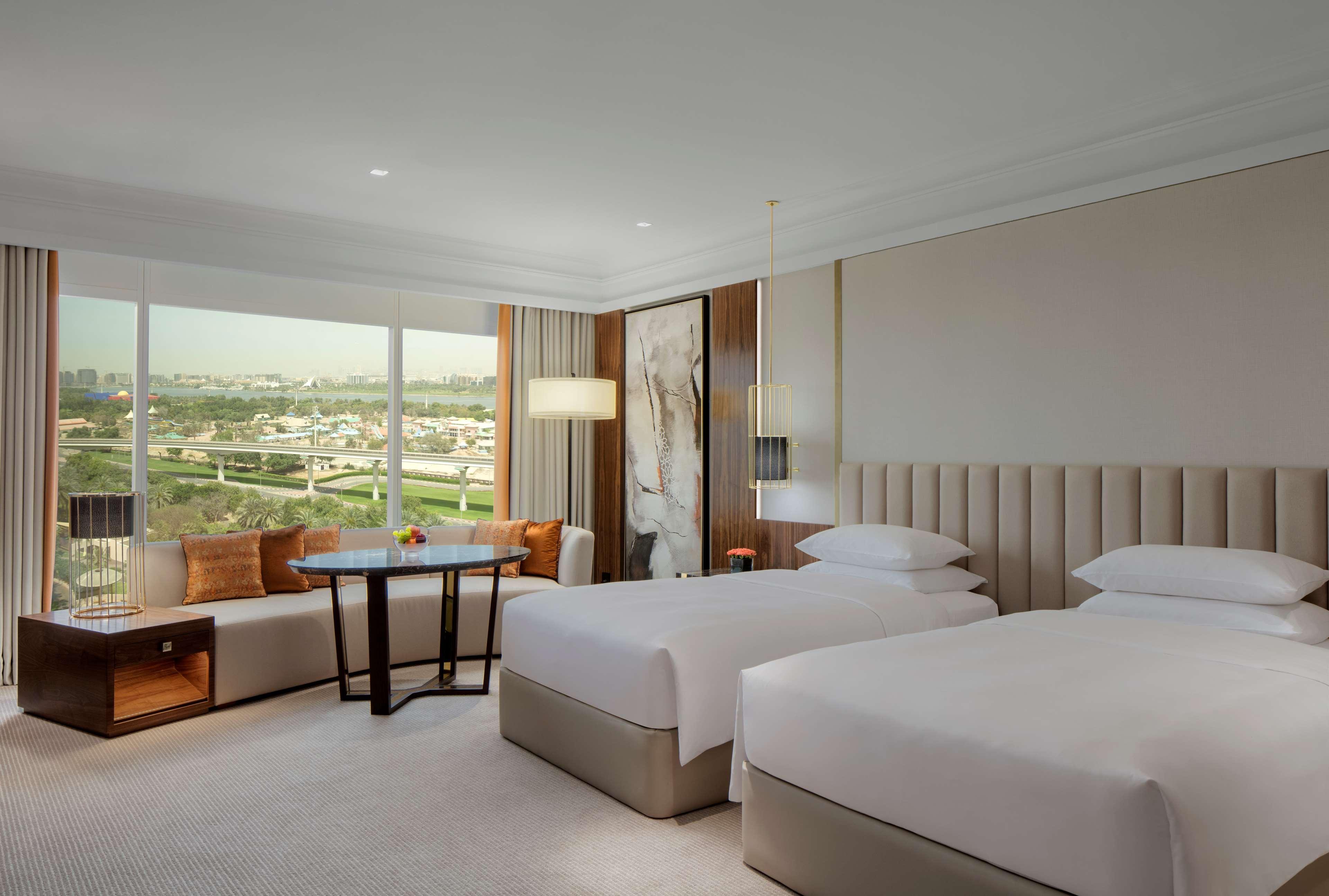 Grand Hyatt Dubai Hotel Exterior photo The photo shows a modern hotel room featuring two twin beds with white bedding. There is a large window providing a view of the outside landscape, allowing natural light to fill the space. The room is decorated in soft, neutral tones with modern furn