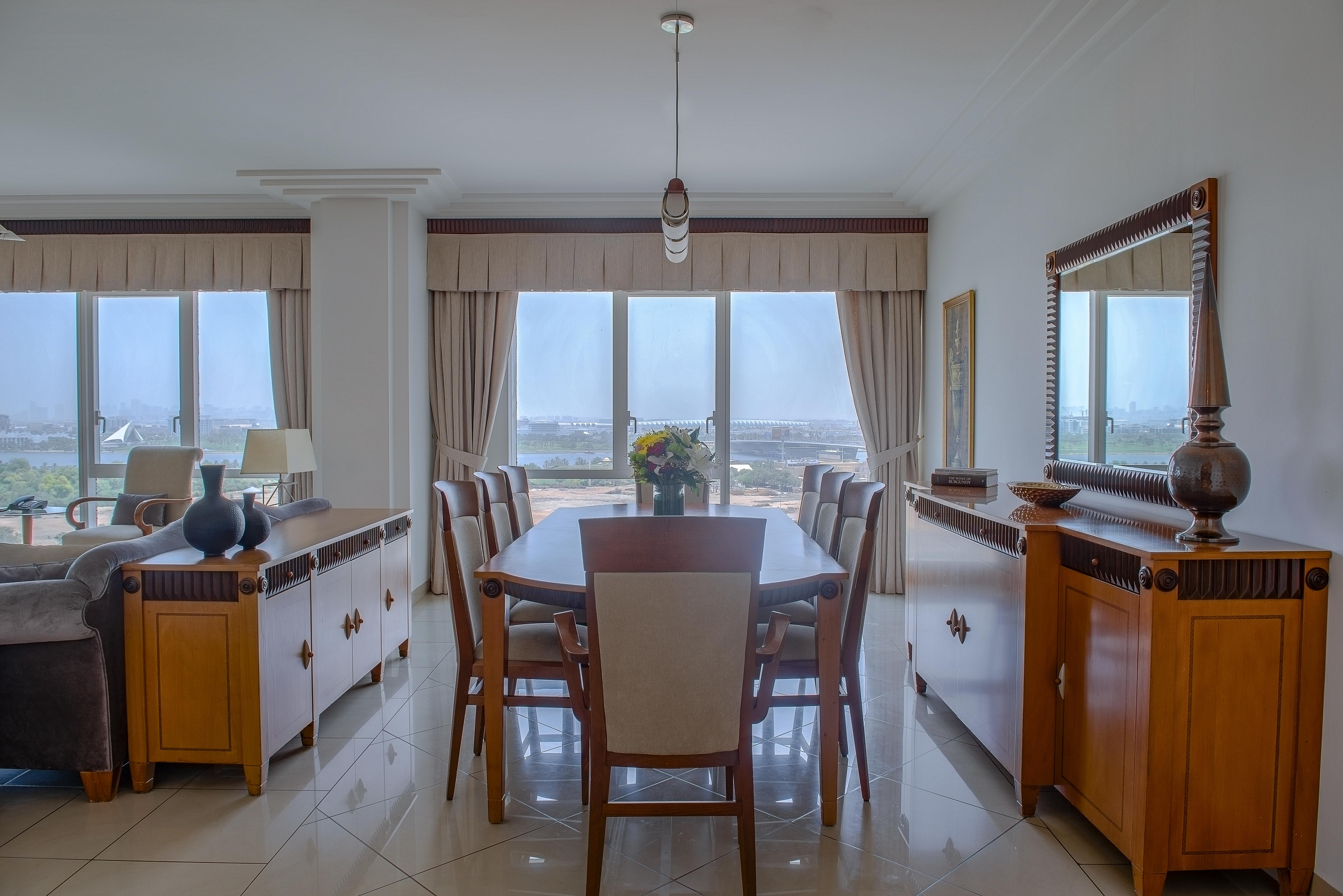 Grand Hyatt Dubai Hotel Exterior photo The photo displays a dining area featuring a stylish wooden dining table surrounded by chairs. The room is bright and airy, with large windows that offer a view of the outdoors. There are beige curtains framing the windows, and the flooring appears t