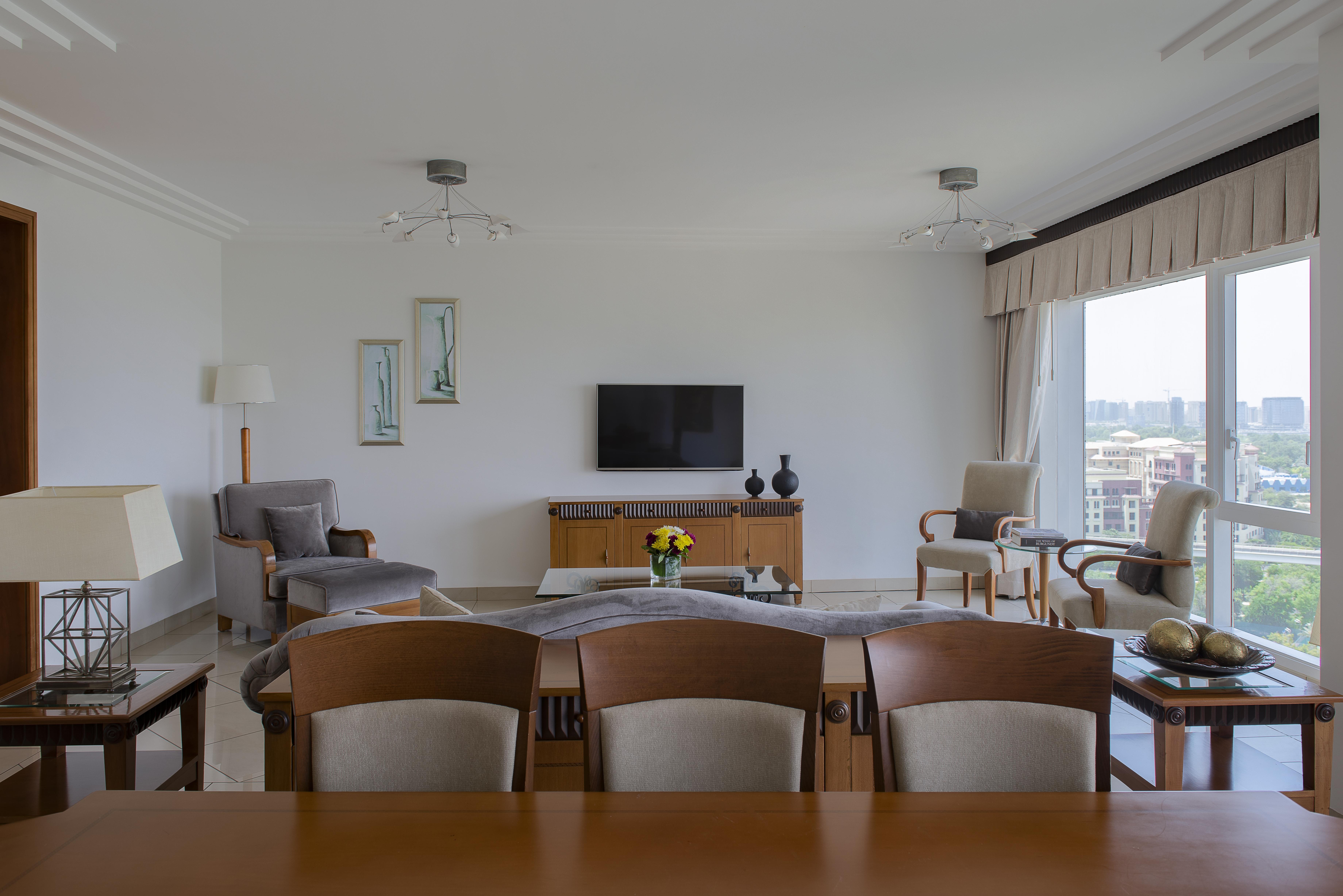 Grand Hyatt Dubai Hotel Exterior photo The photo shows a modern living room with a spacious and minimalistic design. There is a flat-screen television mounted on the wall, facing a seating arrangement that includes two armchairs and a sofa. A wooden table is positioned in the foreground, 