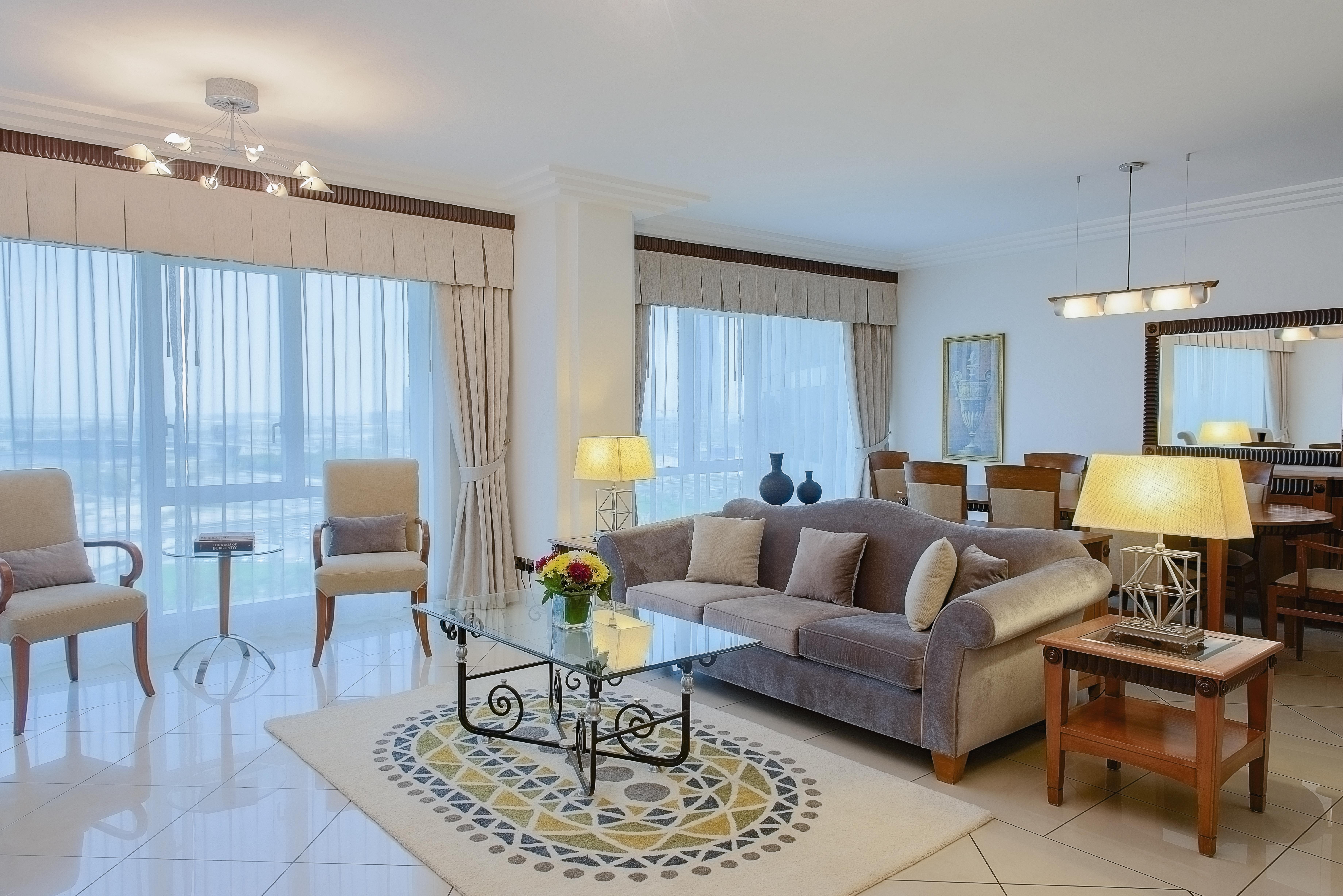 Grand Hyatt Dubai Hotel Exterior photo The photo shows a modern and stylish living room. It features a comfortable beige sofa with decorative pillows, a glass coffee table with an intricate base, and a small side table. There are two armchairs placed beside a floor lamp, creating a cozy s