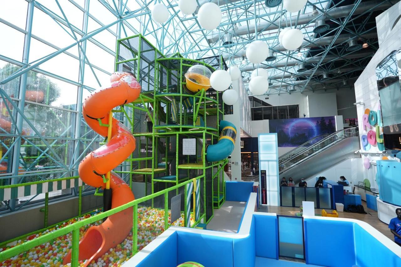 Grand Hyatt Dubai Hotel Exterior photo The photo shows an indoor play area with a modern, colorful design. It features two large water slides—one orange and one blue—leading from a multi-level climbing structure. The climbing structure is surrounded by green framework and includes various