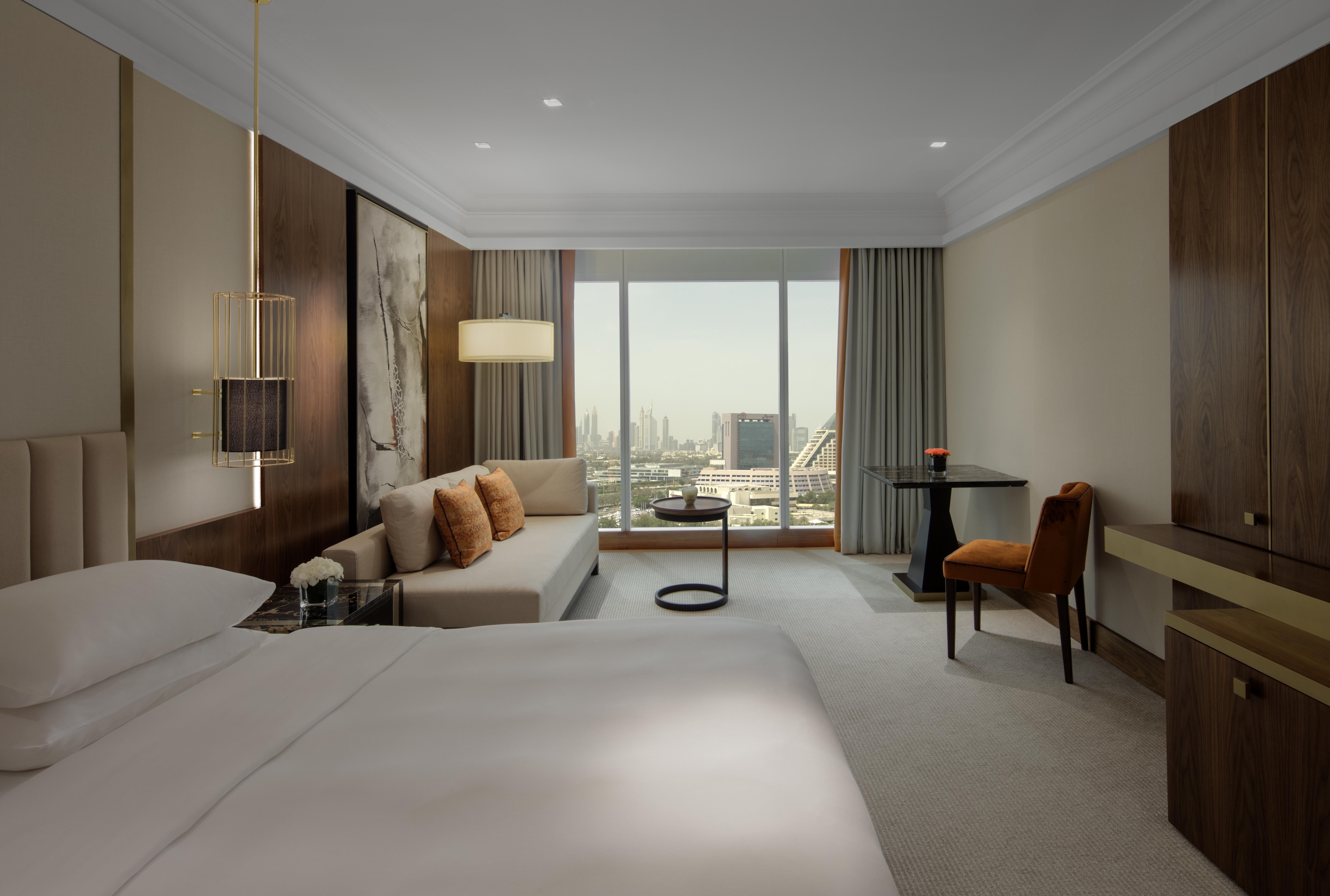 Grand Hyatt Dubai Hotel Exterior photo The photo depicts an elegant hotel room featuring a large bed with white linens. To one side, there is a comfortable sofa adorned with orange cushions, alongside a small round table. A modern chair is situated nearby, creating a cozy seating area. Th
