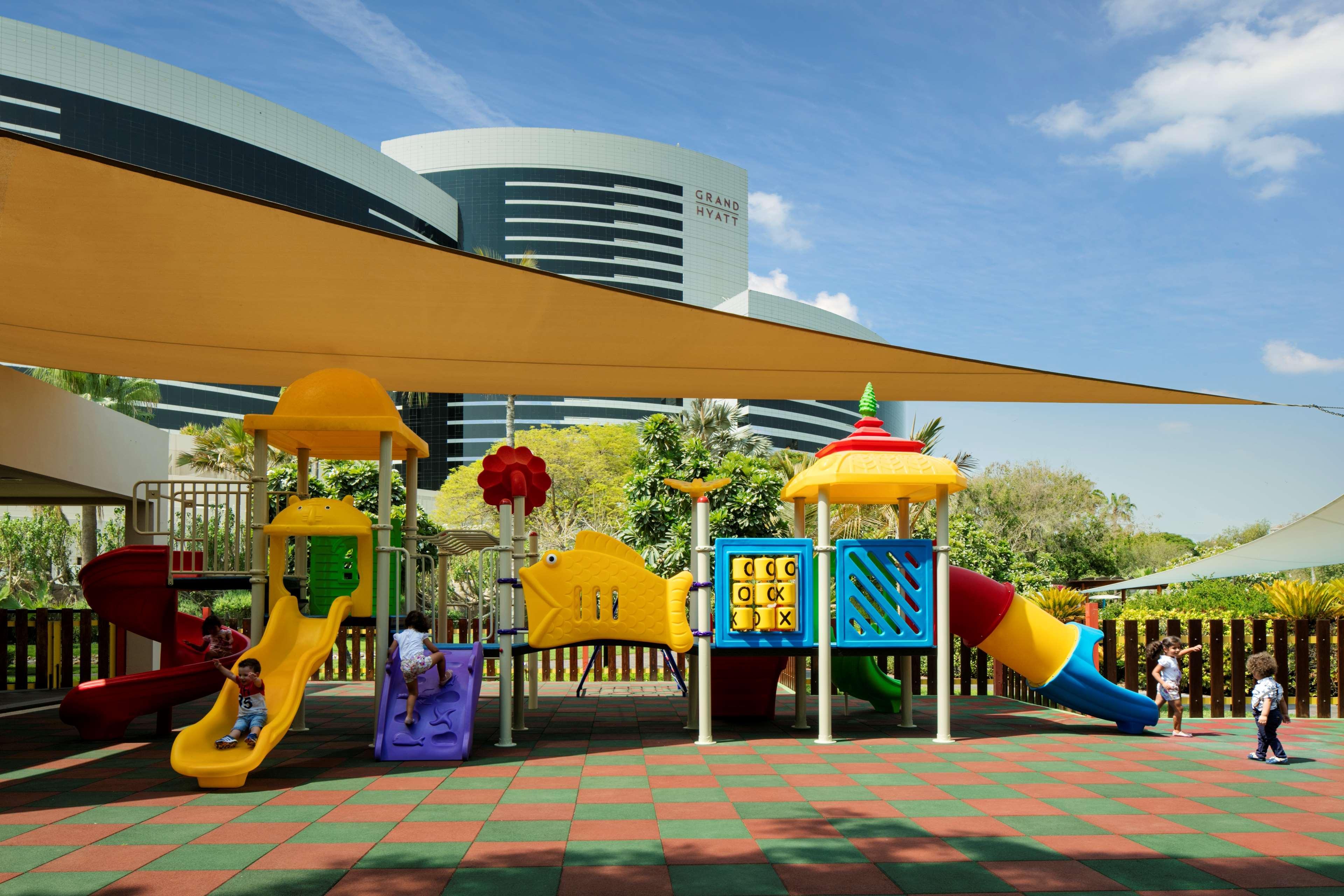 Grand Hyatt Dubai Hotel Exterior photo The image depicts a colorful playground designed for children. It features various play structures, including slides and climbing frames, in vibrant colors such as yellow, purple, and red. There's also a shaded area with a large canopy to protect fro