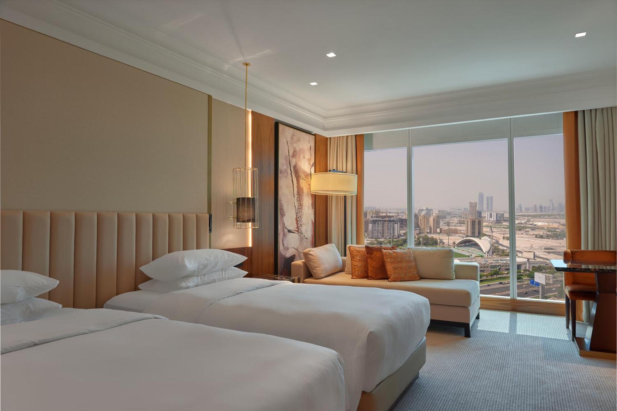 Grand Hyatt Dubai Hotel Exterior photo The photo shows a luxurious hotel room with two twin beds dressed in white linens. The walls are a subtle beige color, and there is a stylish light fixture hanging from the ceiling. A large window offers a view of a cityscape, allowing natural light 