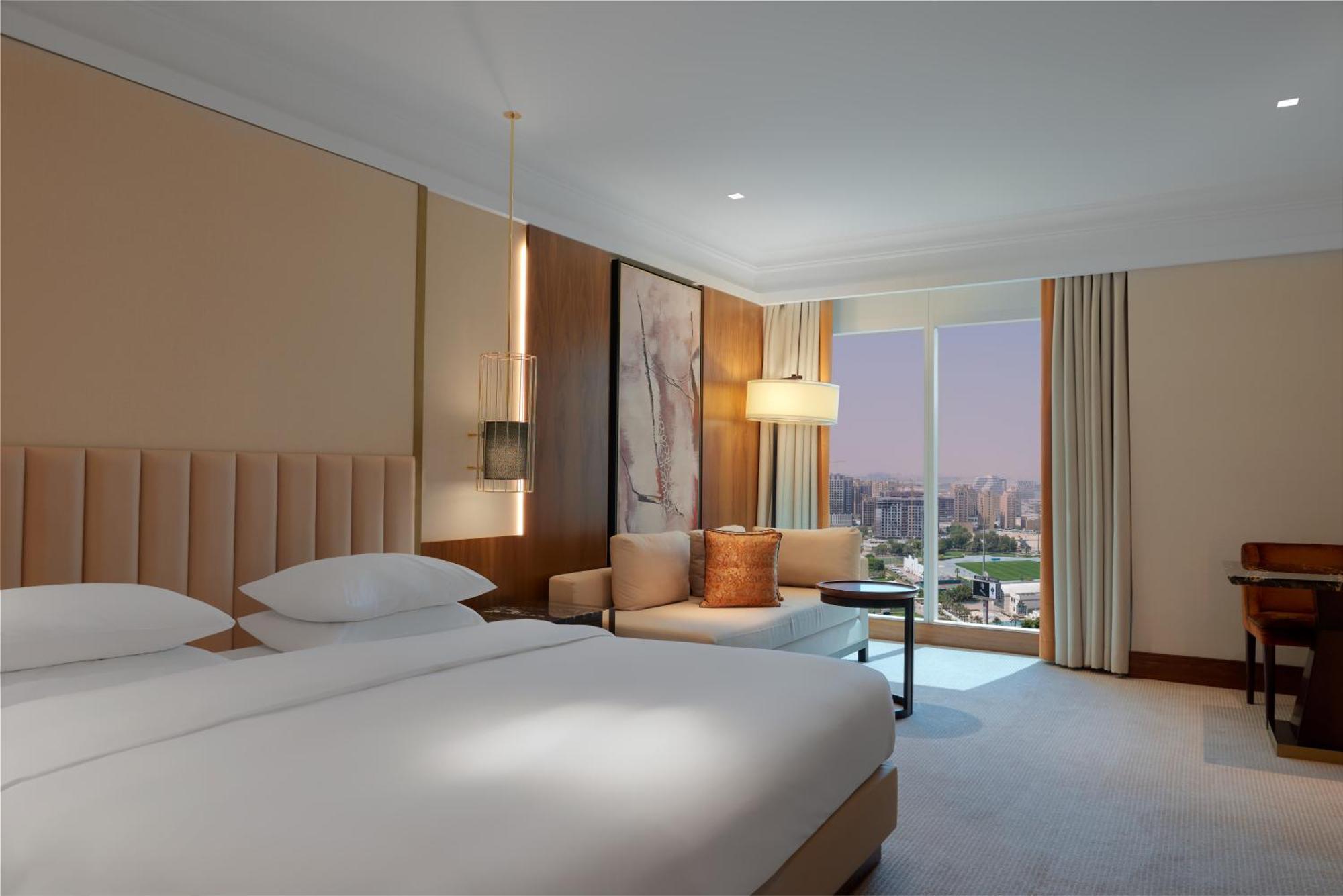 Grand Hyatt Dubai Hotel Exterior photo The image shows a hotel room featuring a modern and elegant design. It includes a large, neatly made bed with white bedding and two pillows at the head. Next to the bed, there's a small side table. On the opposite side, there is a comfortable seating