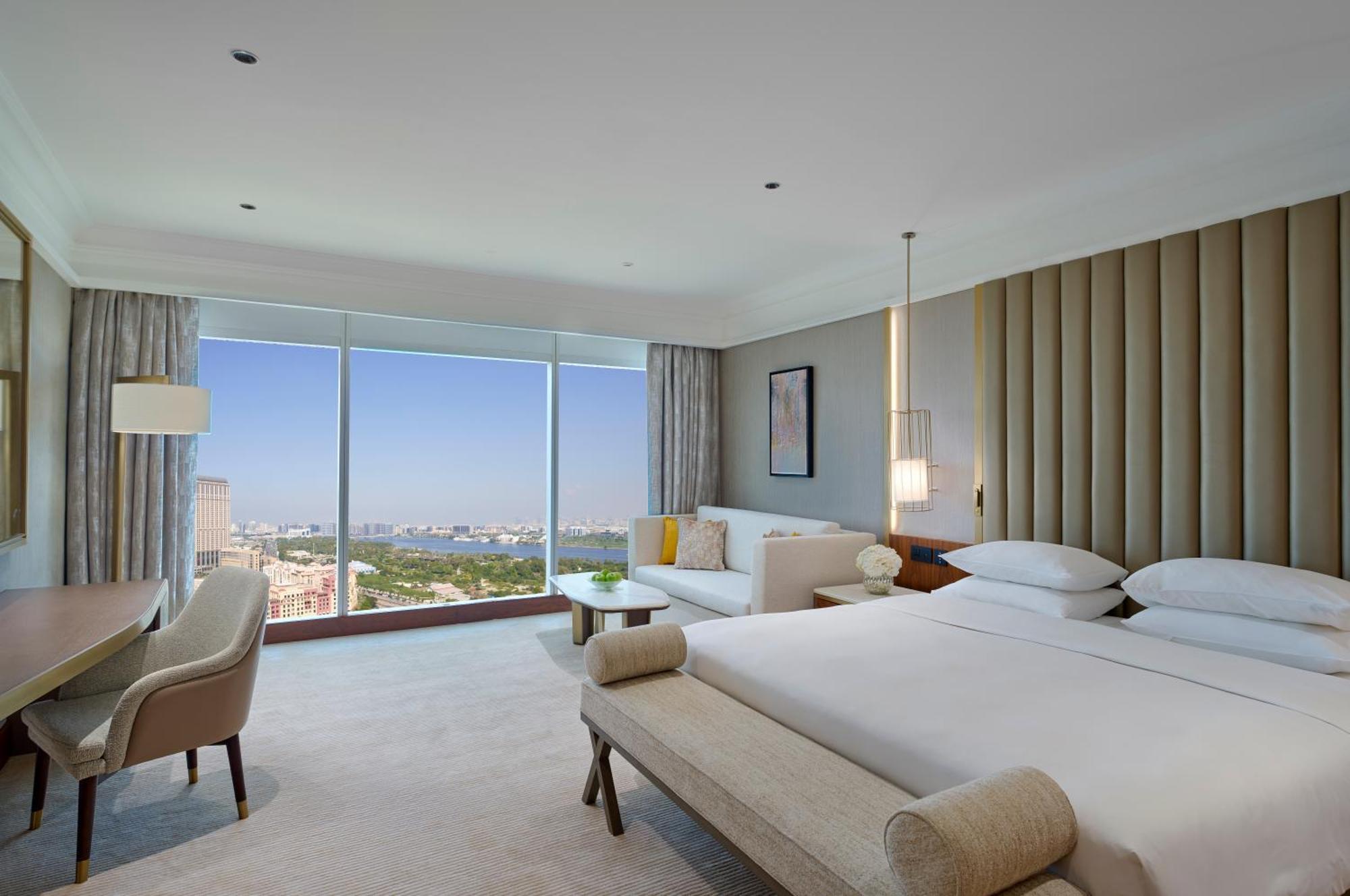 Grand Hyatt Dubai Hotel Exterior photo The photo shows a modern hotel room featuring large windows with a view. The room is designed with a neutral color palette and elegant furnishings. There are two beds neatly made, a sofa area, and a small table. Soft lighting fixtures are present, an