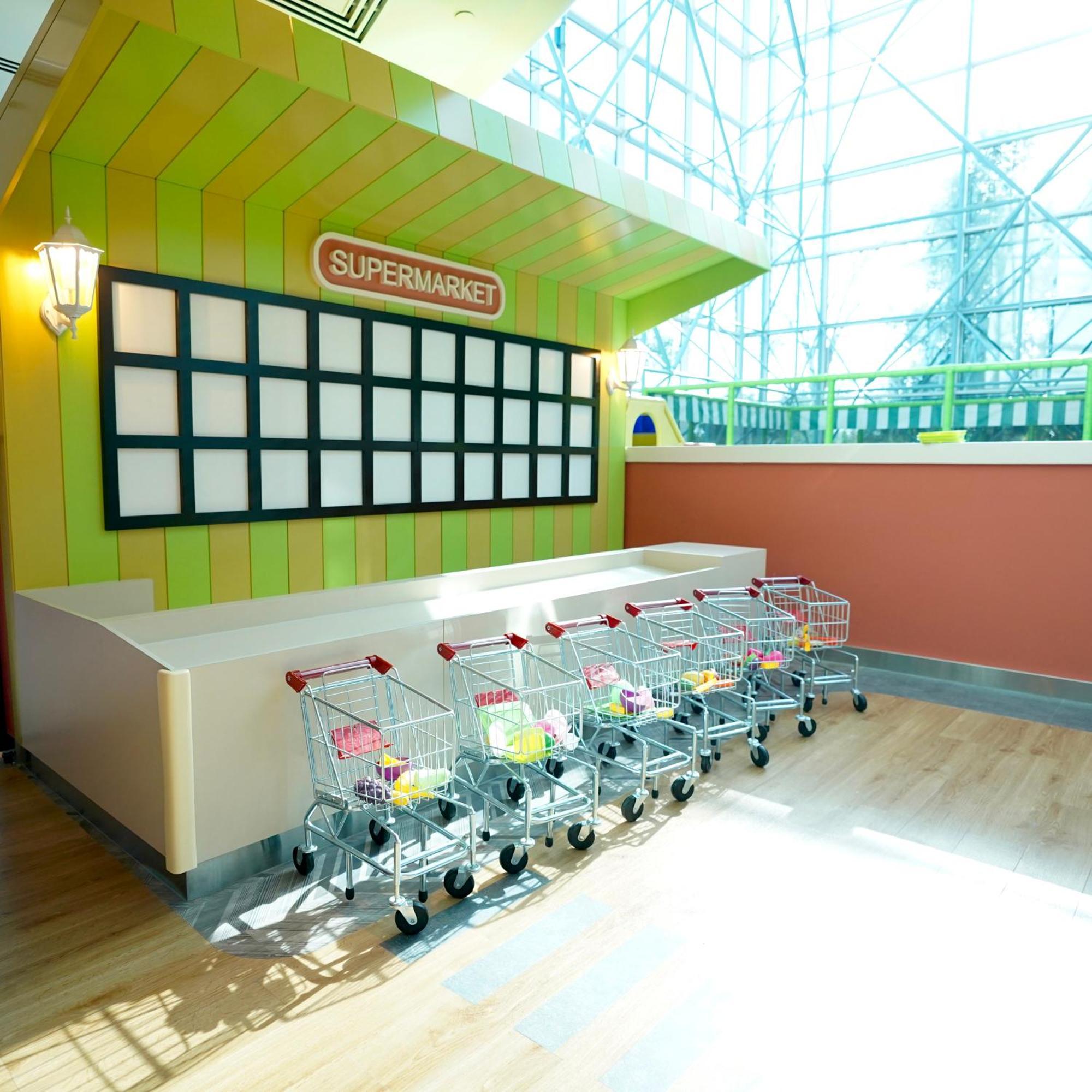 Grand Hyatt Dubai Hotel Exterior photo The photo shows a miniature supermarket area, designed for children. It features a colorful, playful setting with a green and yellow striped backdrop and a sign that reads "SUPER MARKET." There are several small shopping carts lined up in front of a 