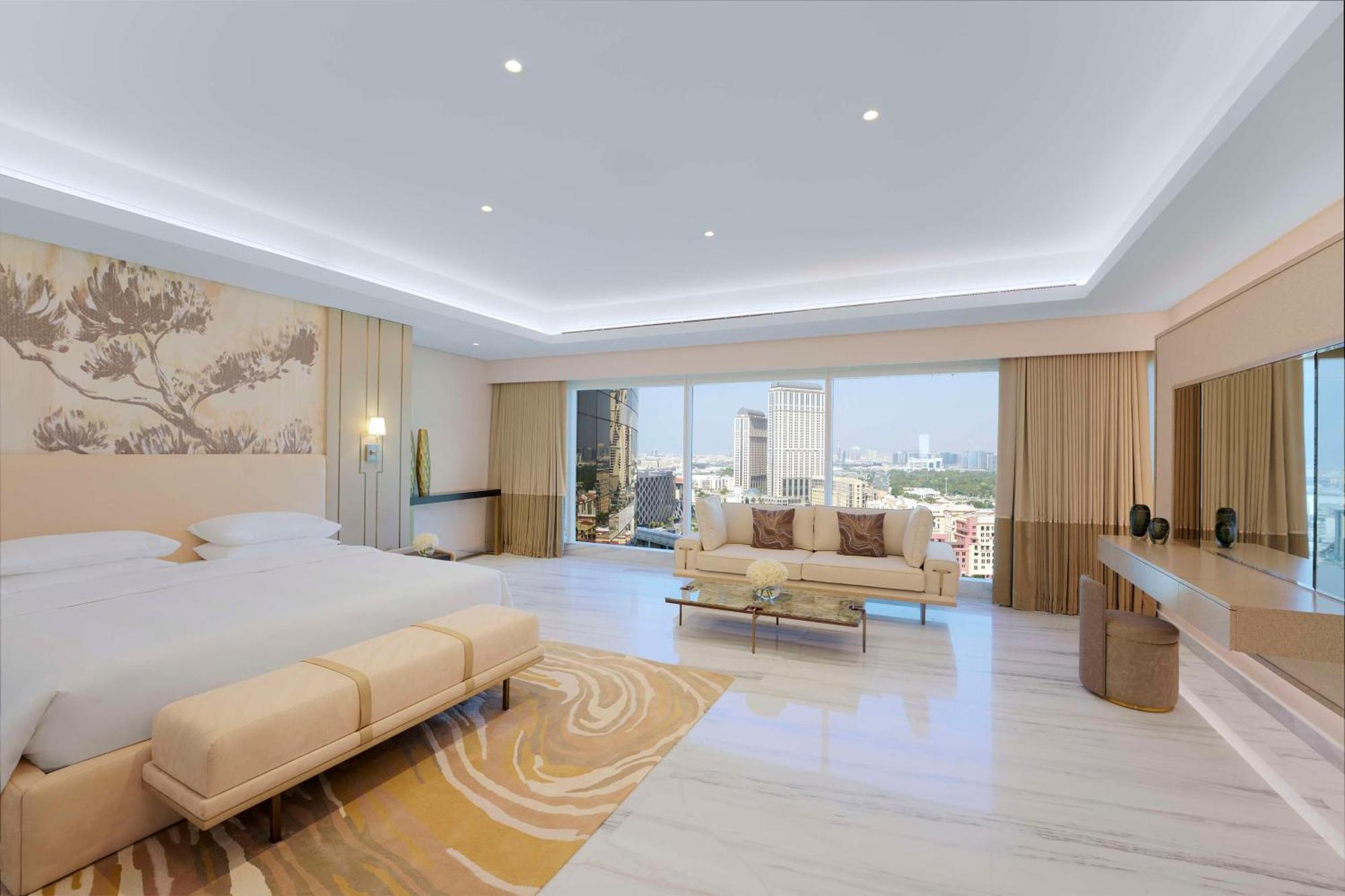 Grand Hyatt Dubai Hotel Exterior photo The image shows a spacious hotel room that features a contemporary design. It has a large window that offers a view of the city skyline, allowing natural light to fill the space. The room includes a cozy seating area with a light-colored sofa and a s