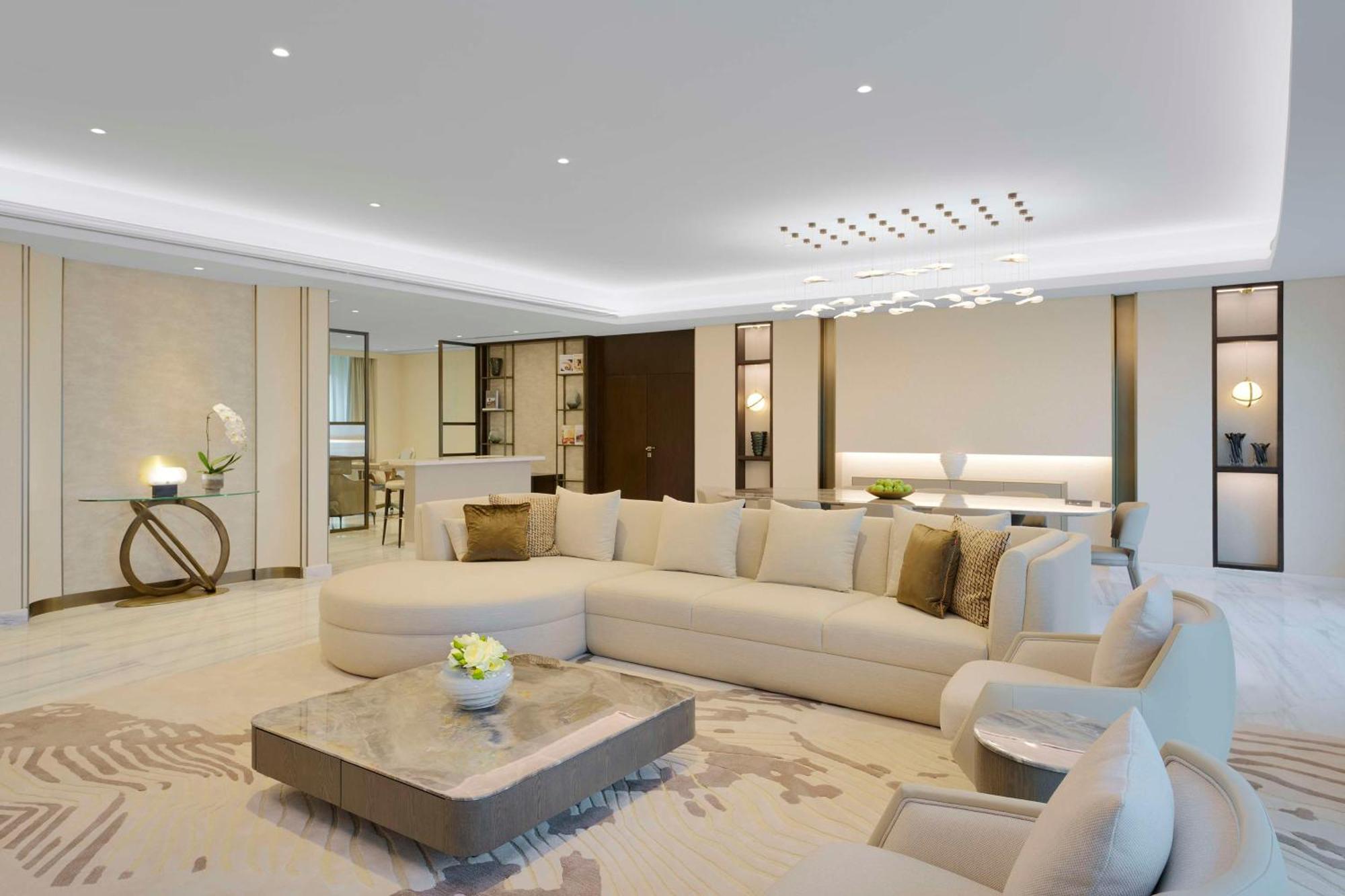 Grand Hyatt Dubai Hotel Exterior photo The photo depicts a modern and luxurious living room. A large, L-shaped, light-colored sectional sofa occupies a central position, adorned with a few decorative pillows. In front of the sofa is a stylish coffee table that features a smooth surface, p