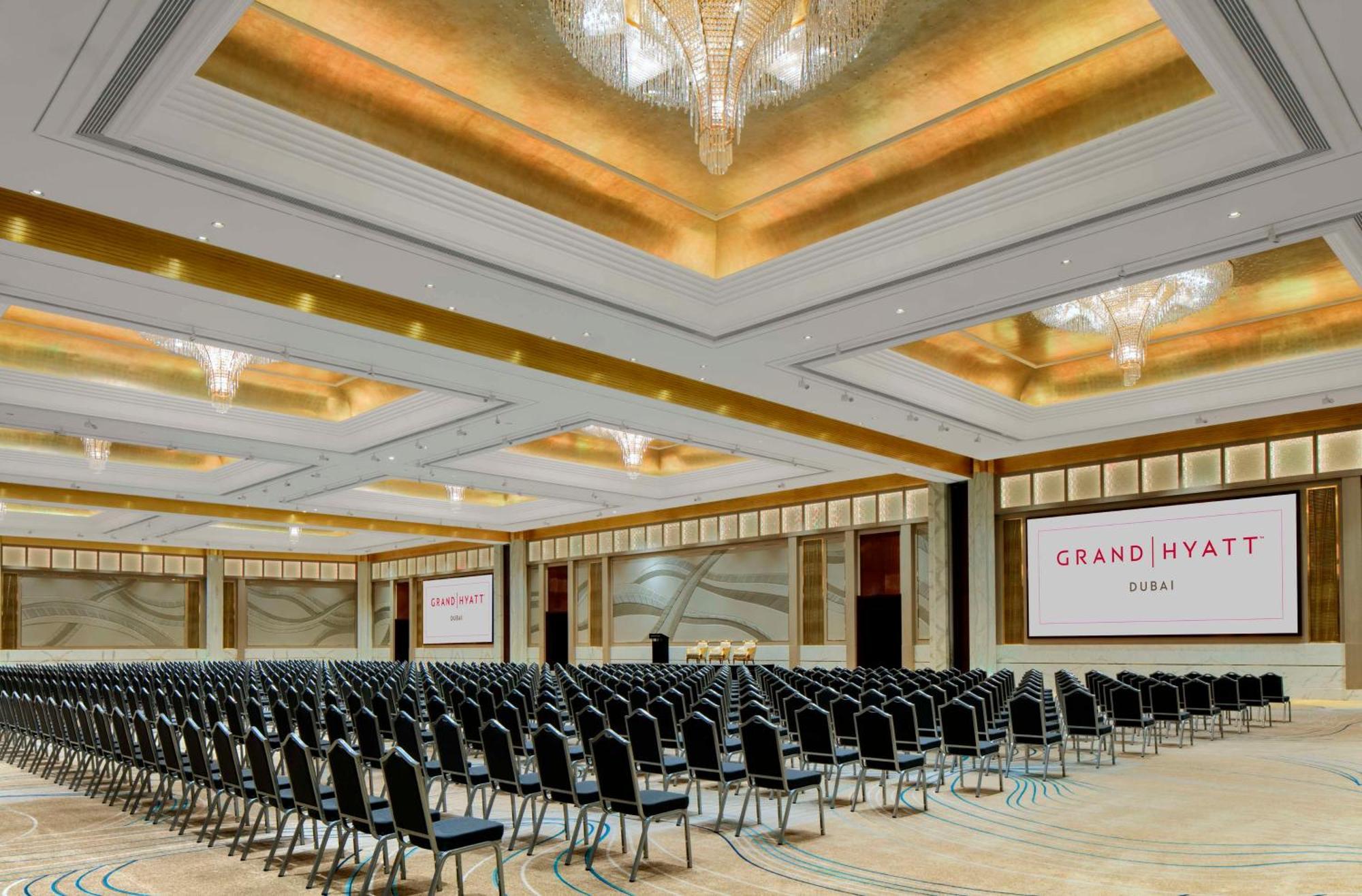 Grand Hyatt Dubai Hotel Exterior photo The photo shows a large, elegantly designed conference room at the Grand Hyatt hotel. The room features rows of black chairs arranged for an event, indicating it is set up for an audience. The ceiling has a decorative design with chandeliers that pro