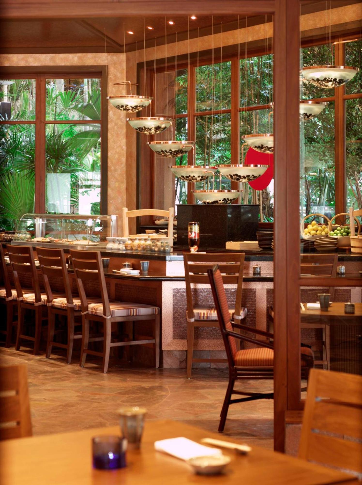 Grand Hyatt Dubai Hotel Exterior photo The photo shows the interior of a restaurant or dining area with a warm and inviting ambiance. There is a long wooden bar with several empty chairs arranged in front of it. The bar features sleek, modern light fixtures hanging above, and there are va