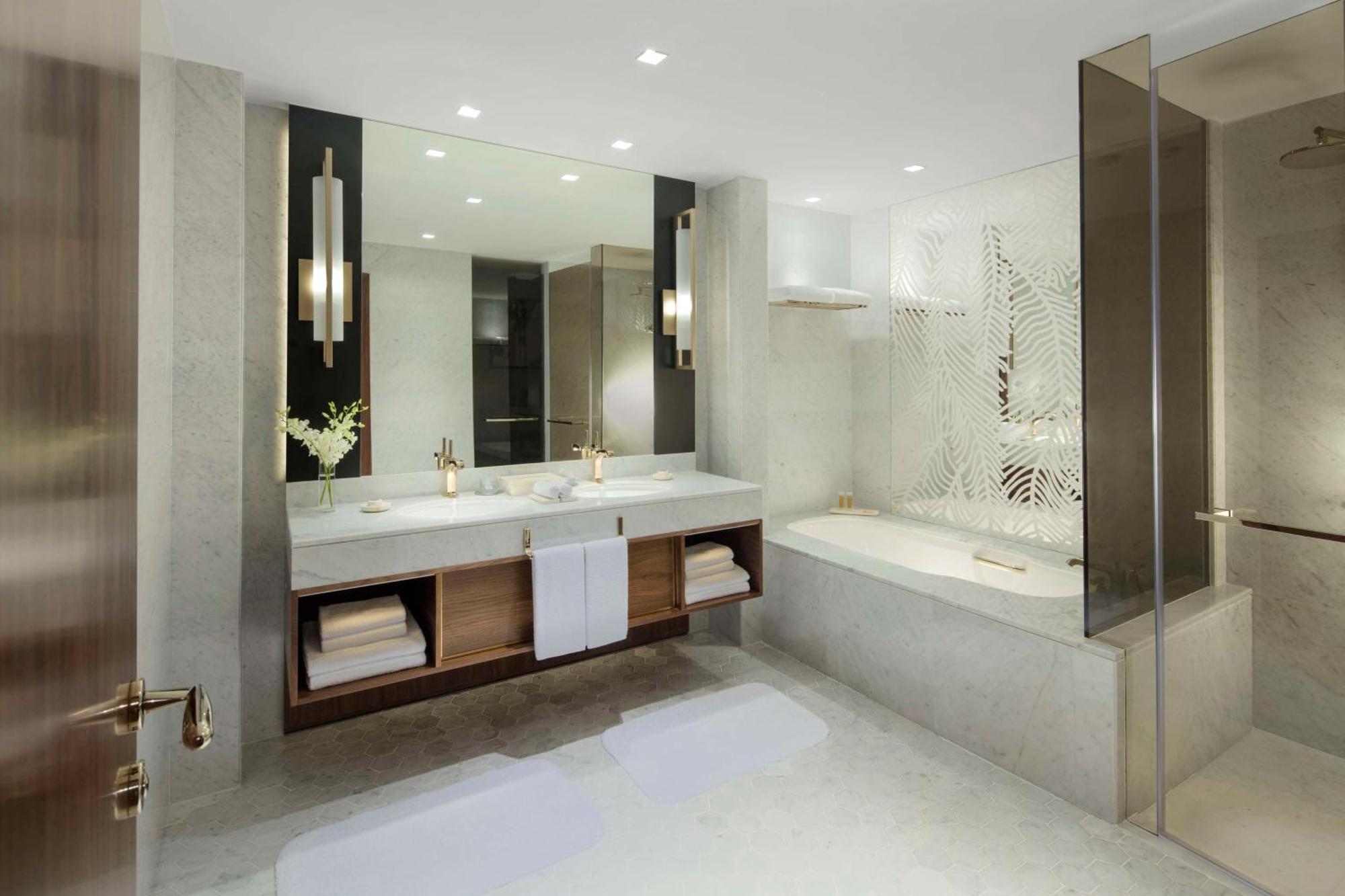 Grand Hyatt Dubai Hotel Exterior photo The photo shows a modern bathroom design featuring a sleek and minimalist aesthetic. It includes:

- A large, double vanity with a white countertop and two sinks, enhanced by stylish gold faucets.
- Above the vanity, there is a spacious mirror that r