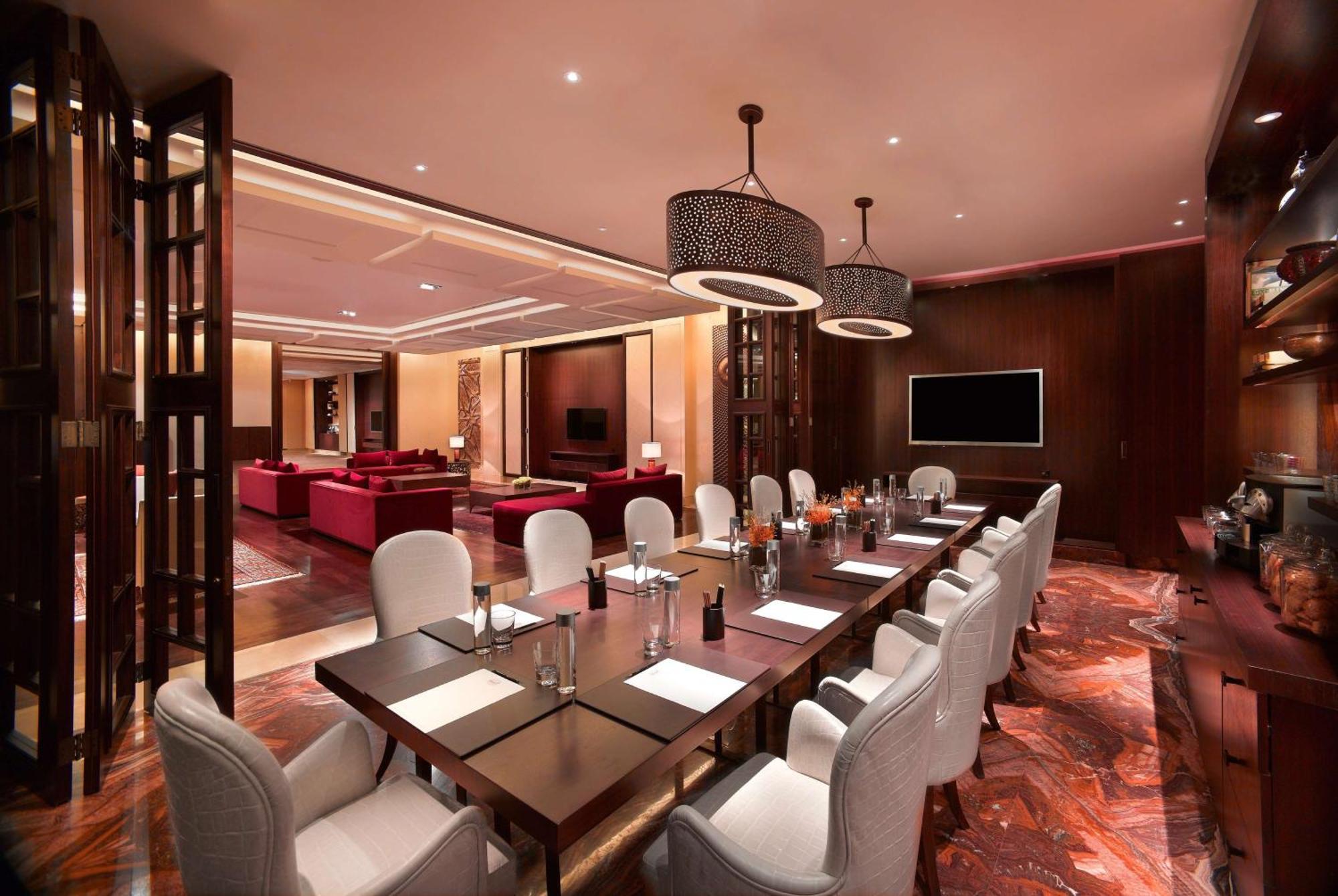 Grand Hyatt Dubai Hotel Exterior photo The photo shows an elegant dining or conference room. It features a long wooden table surrounded by white, upholstered chairs. The table is set with notepads and pens, indicating it may be used for meetings. There are two stylish light fixtures hangi