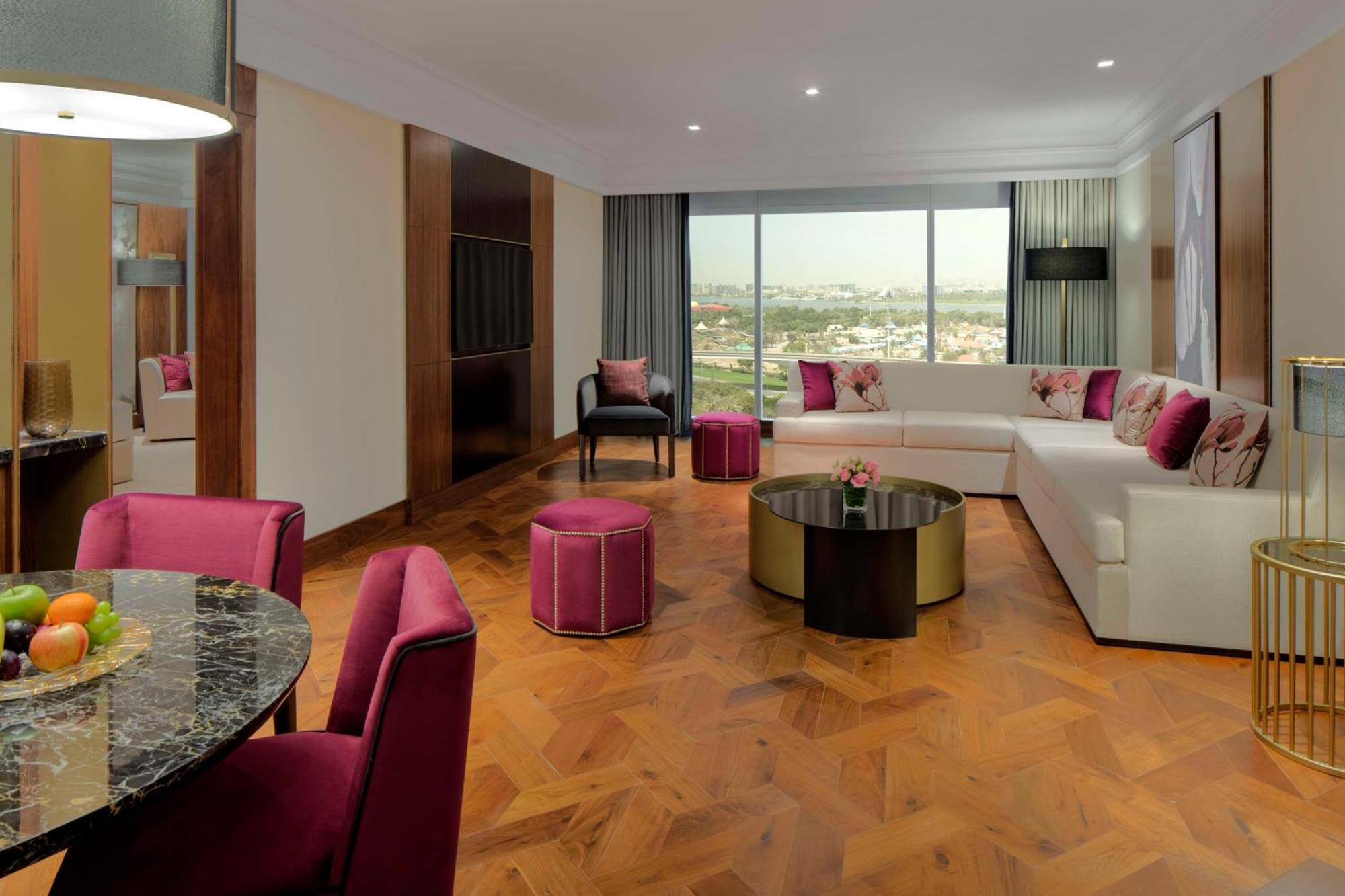 Grand Hyatt Dubai Hotel Exterior photo The photo shows a modern and stylish living space. There is a large, L-shaped white sofa adorned with pink and purple cushions, complemented by a round black coffee table in the center. In front of the sofa, there are two round ottomans in a matching